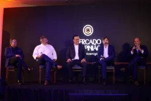 Cinco homens de terno participam de painel de debates sentados no palco do evento Mercado & Opinião, com um deles falando ao microfone.