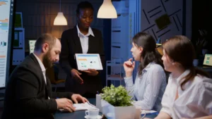 Empresária apresenta gráficos em tablet para equipe diversa durante reunião de negócios em escritório moderno.