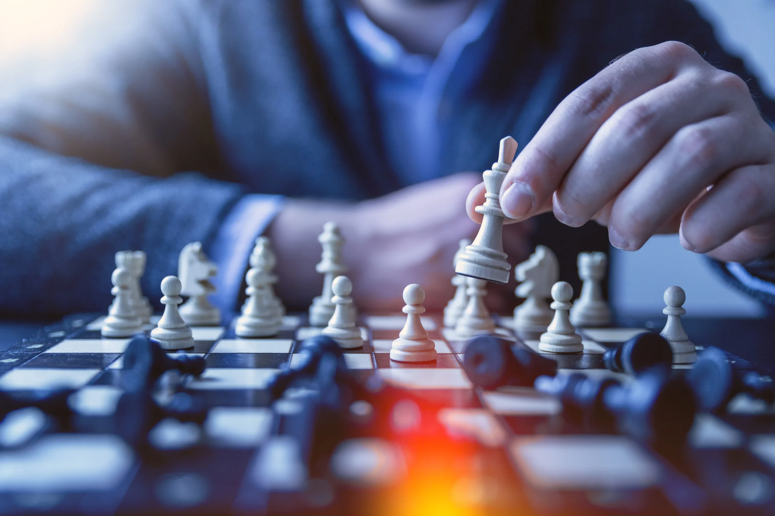 Mão de homem movimentando peça de xadrez branca em tabuleiro, representando estratégia e tomada de decisão.